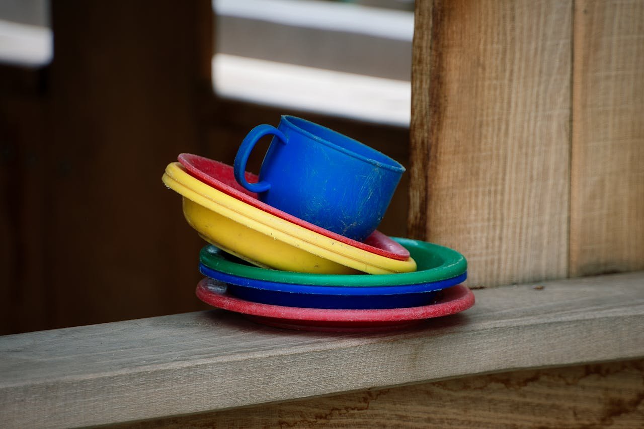 gallery-5 Vibrant colored plastic dishes and cup on wooden ledge, creating an artistic and playful scene.
