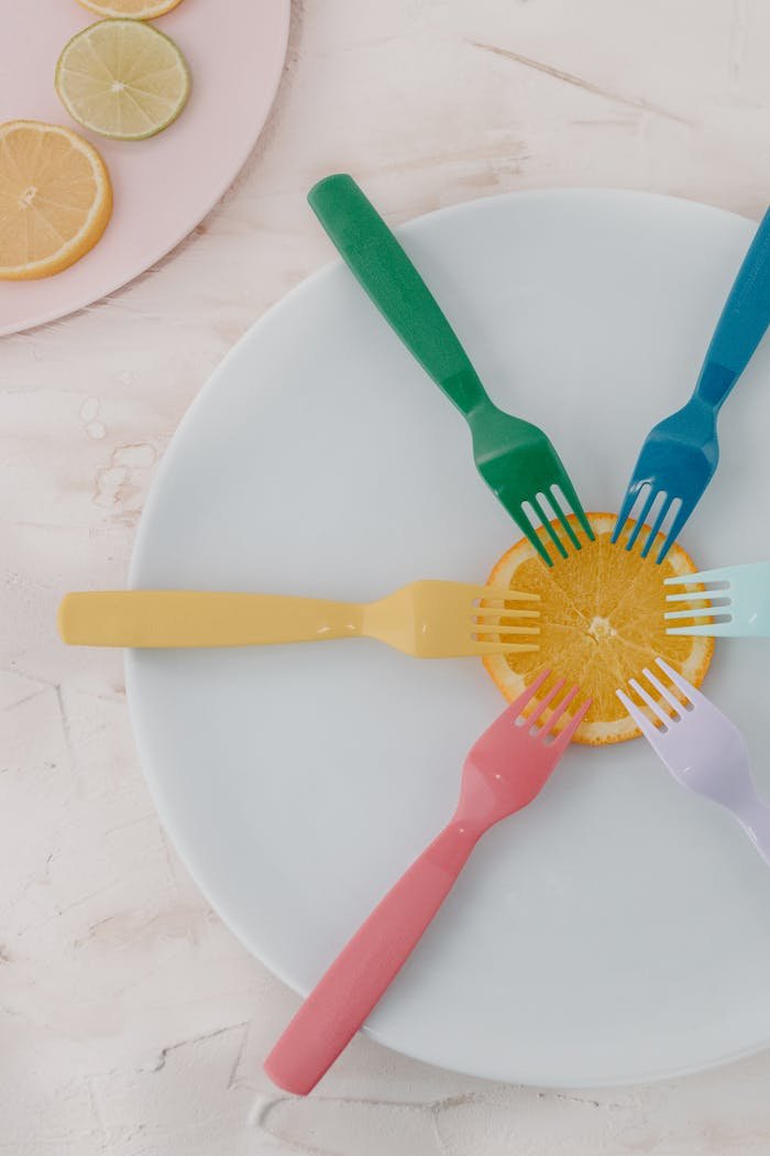 why-choose-us Flat lay of colorful forks on an orange slice on a white plate, perfect for food and creativity themes.