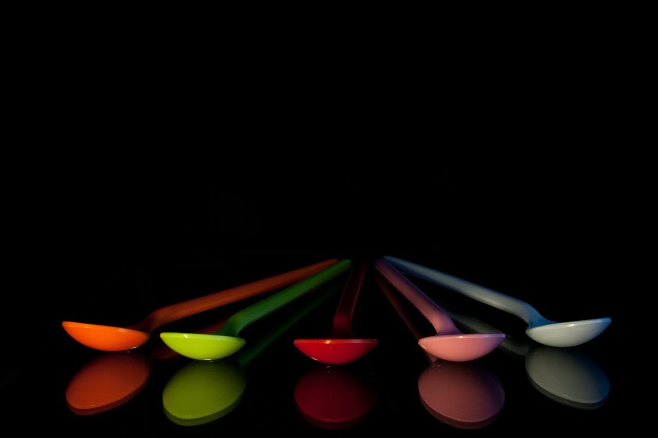 gallery-4 A set of colorful plastic spoons reflected on a black surface with a striking contrast.